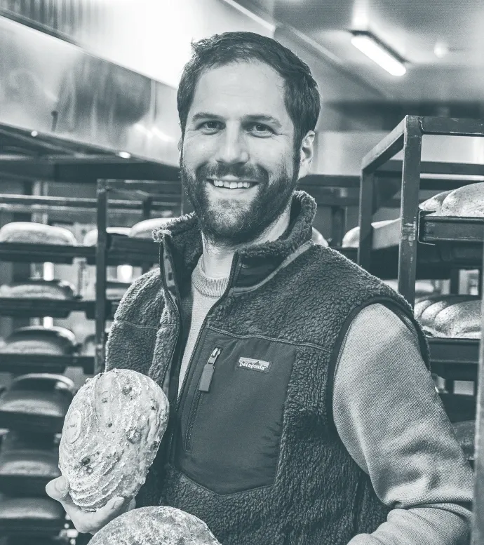 A Walloon baker holding a loaf in his bakery